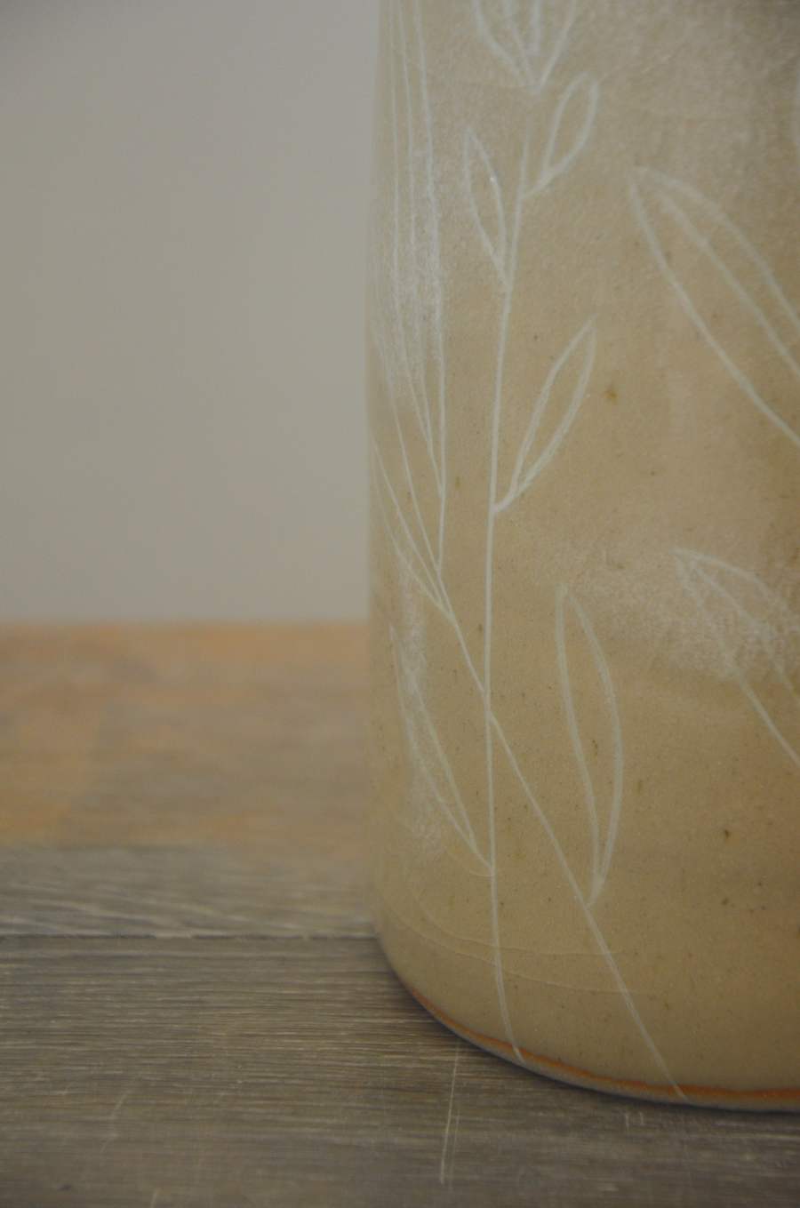 Détail de feuillages blancs sur la paroi d'un vase beige.