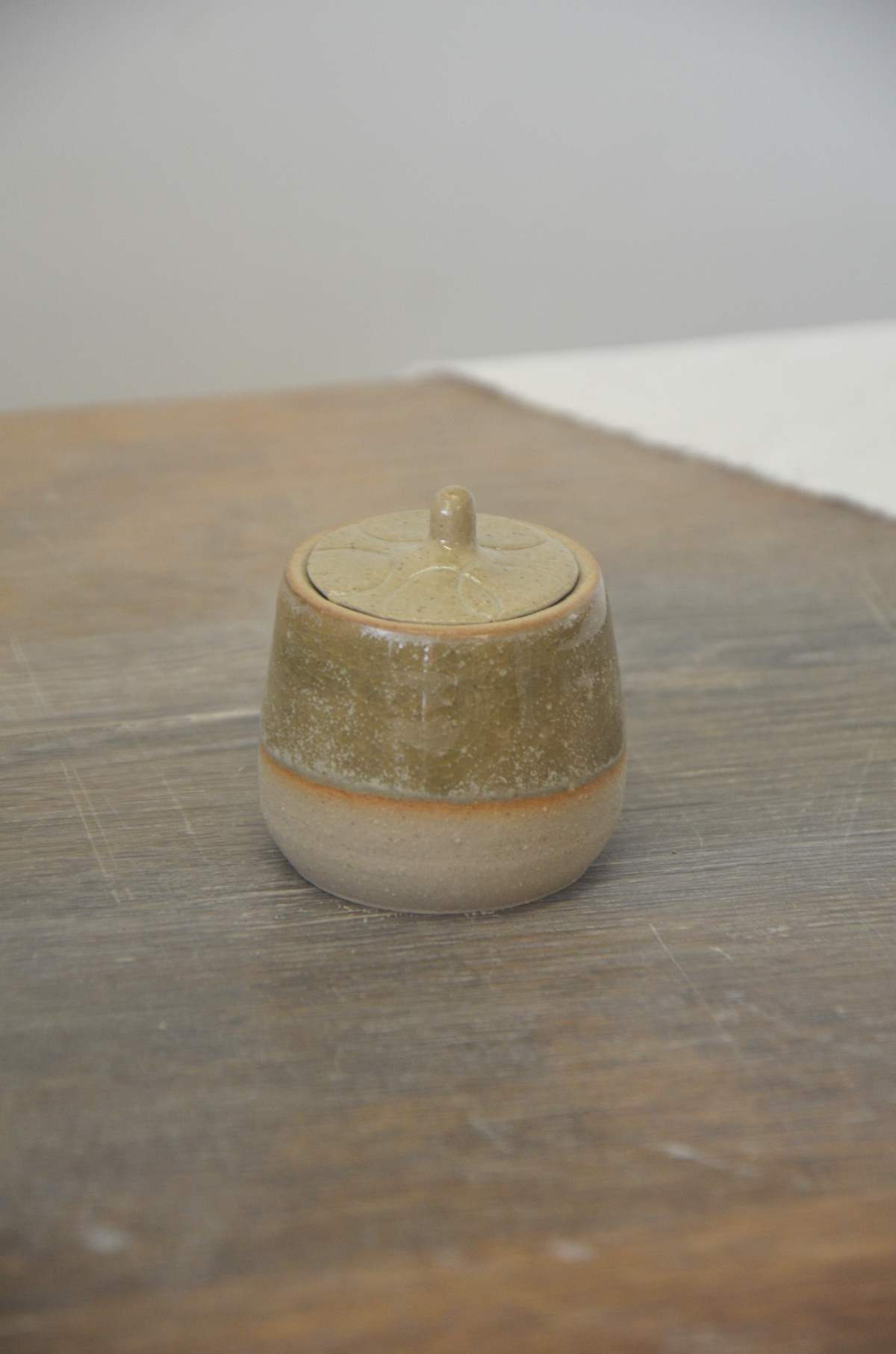 Petit pot à couvercle vert-brun sur une table en bois.