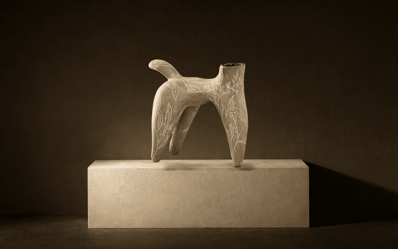 Sculpture à quatre pattes gravée de feuillages, posée sur un bloc enduit, éclairée de la gauche
